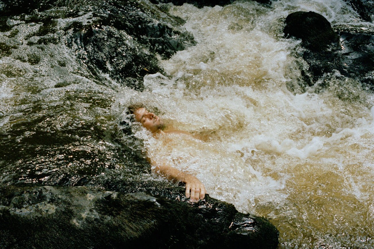Ein Mann liegt auf dem Rücken, während das Wasser über die Felsen und Wasserfälle strömt.