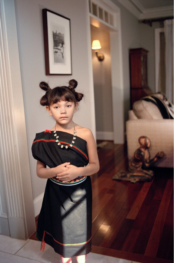 Ein junges Mädchen steht in einem Wohnzimmer und trägt ein traditionelles Hopi-Kleid.
