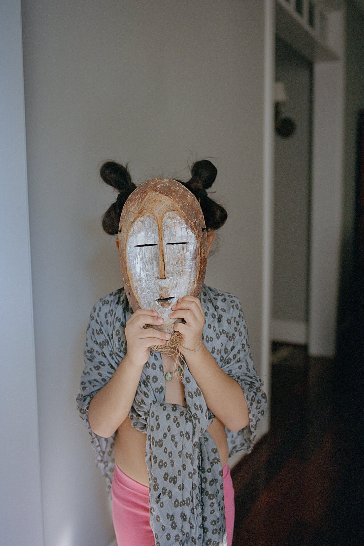 Ein junges Mädchen hält eine traditionelle Maske vors Gesicht.