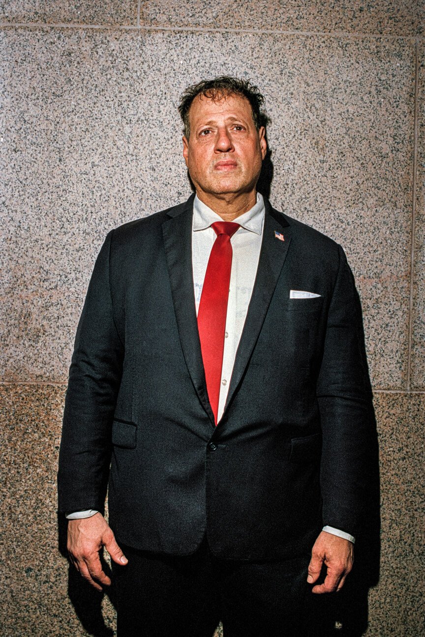 Ritratto dall'alto di uomo di grossa corporatura che indossa un abito nero e una cravatta rossa.