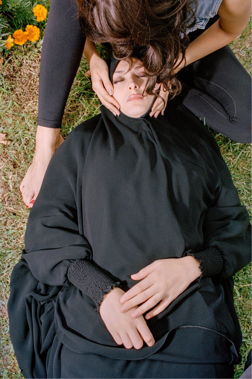 Eine Person hält das Gesicht einer verschleierten Frau, die im Gras liegt.