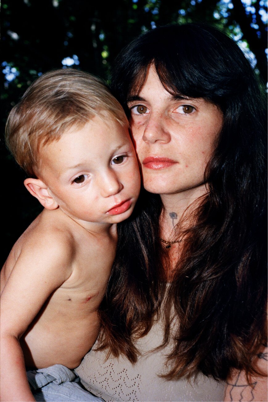 Ein Porträt einer Frau, die ein Kind hält, mit neutralem Gesichtsausdruck.