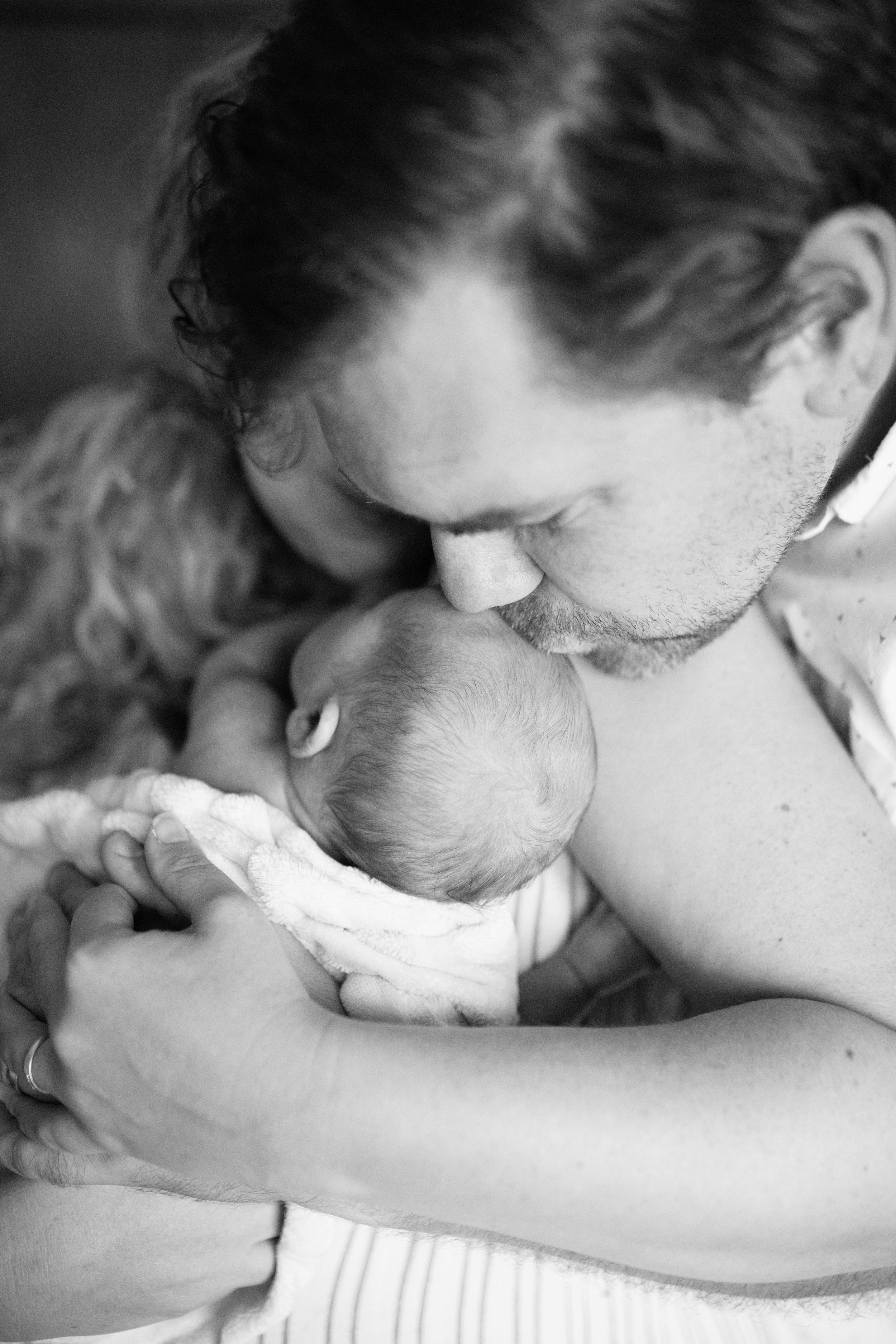 A black-and-white photo of a man tenderly holding a newborn baby close to his face, with the man gently kissing the baby's head.