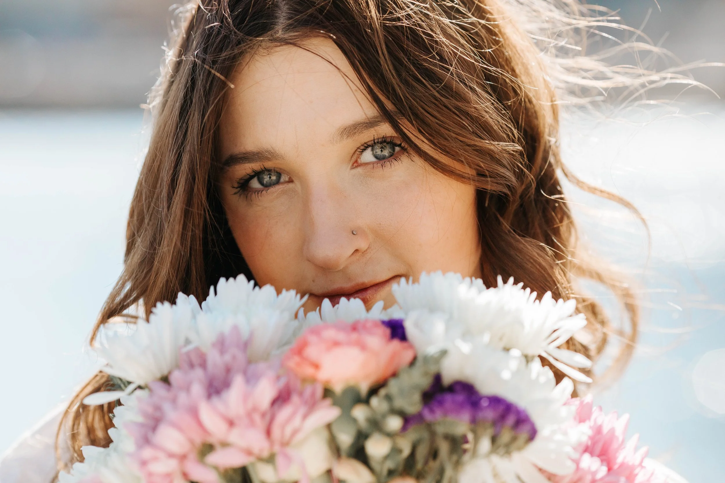 Close-up portrait of a woman with blue eyes and wavy brown hair holding a colorful bouquet of flowers.