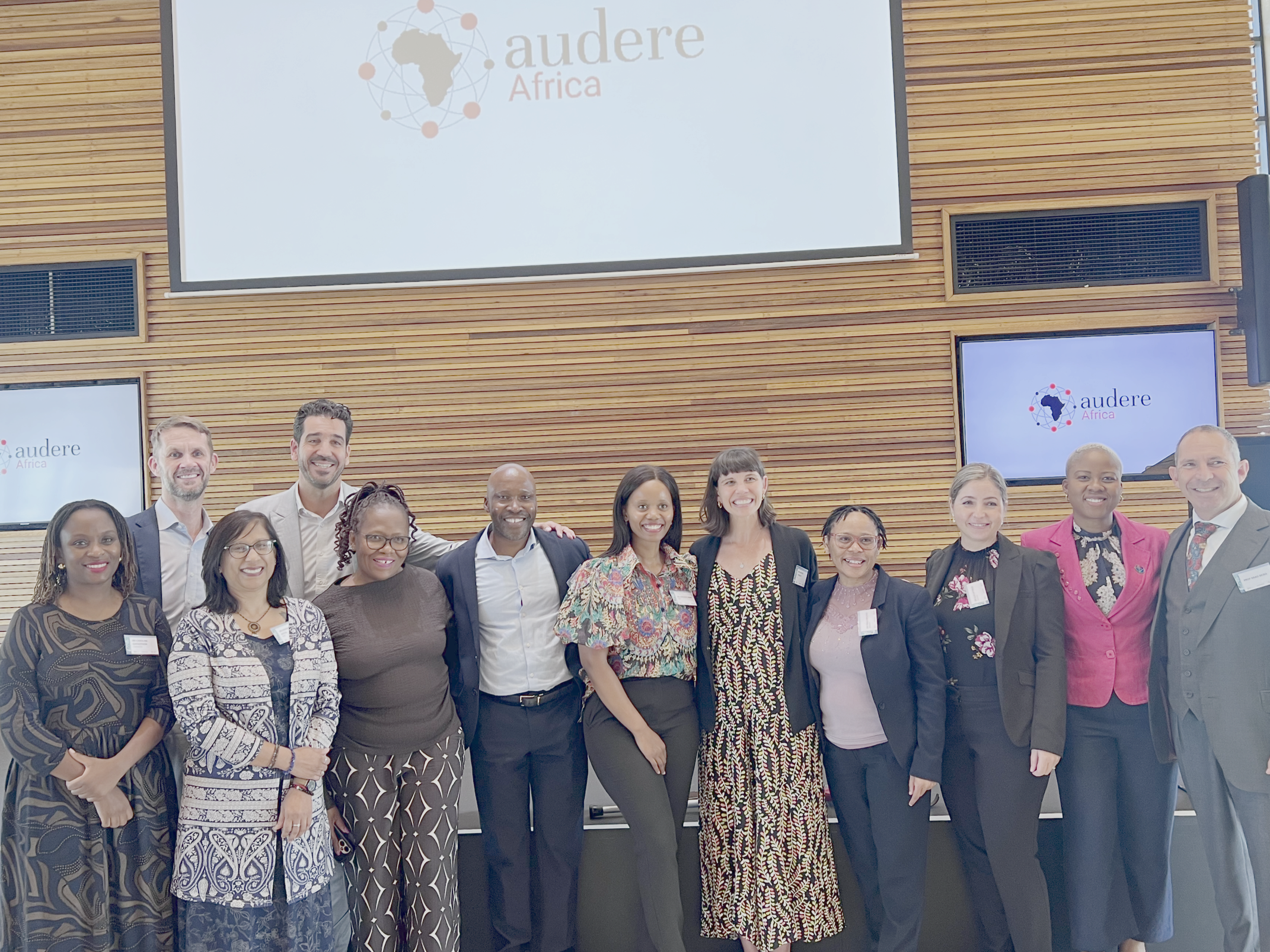 A group of people in front of an Audere Africa logo on a screen