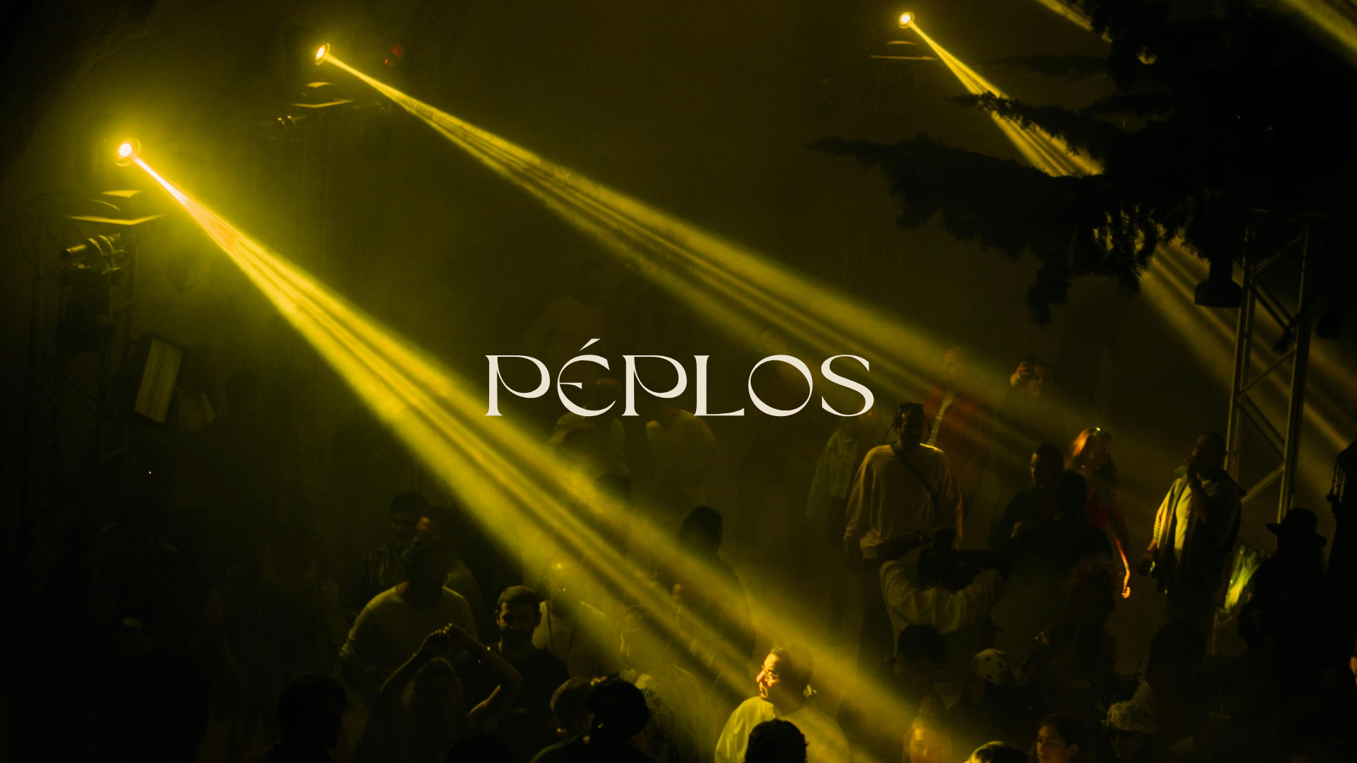 People gathered in a dark area illuminated by yellow stage lights, with the word 'PEPLOS' overlaid in white text.