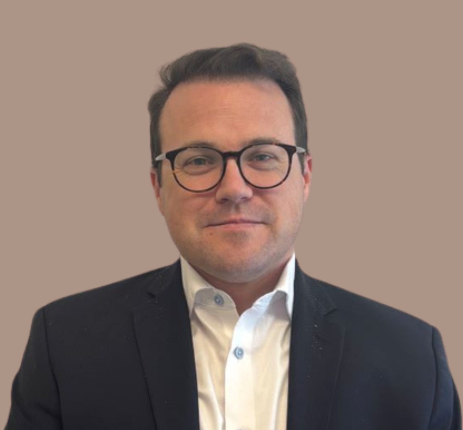 A middle aged man with short brown hair and blue eyes is shown looking at the camera. The man, Jacob, is wearing rounded glasses, a navy suit jacket, and a white button up with light blue buttons.