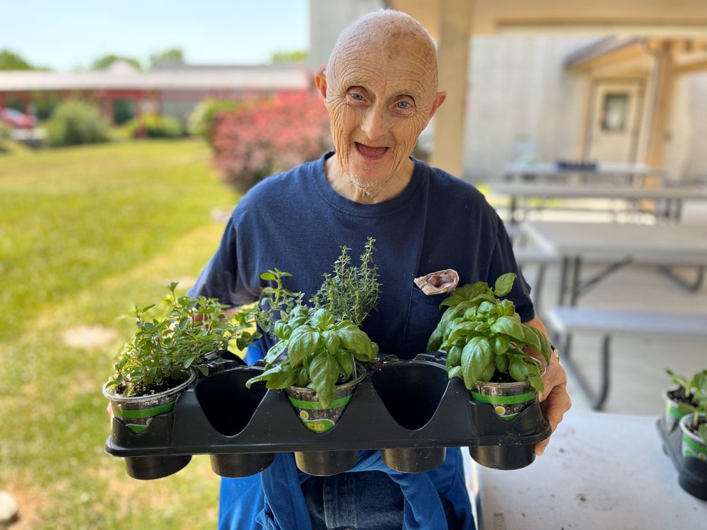  A man holding up a carton of various plants is smiling at the camera. 