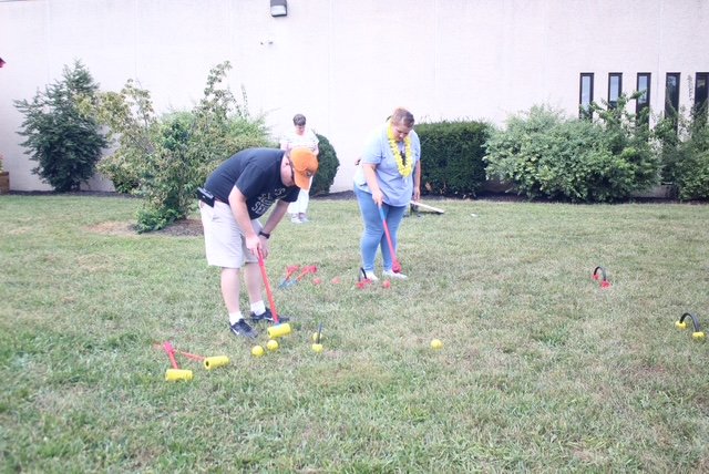  A young man and woman stand in the grass and play a game of croquet. 