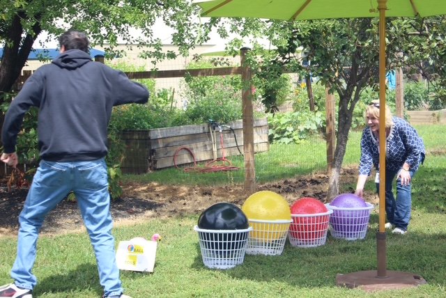  A man with his back to the camera is shown and a  middle aged woman is shown halfway bent down and checking on a row of balls that are all placed in their own laundry basket to hold them. 