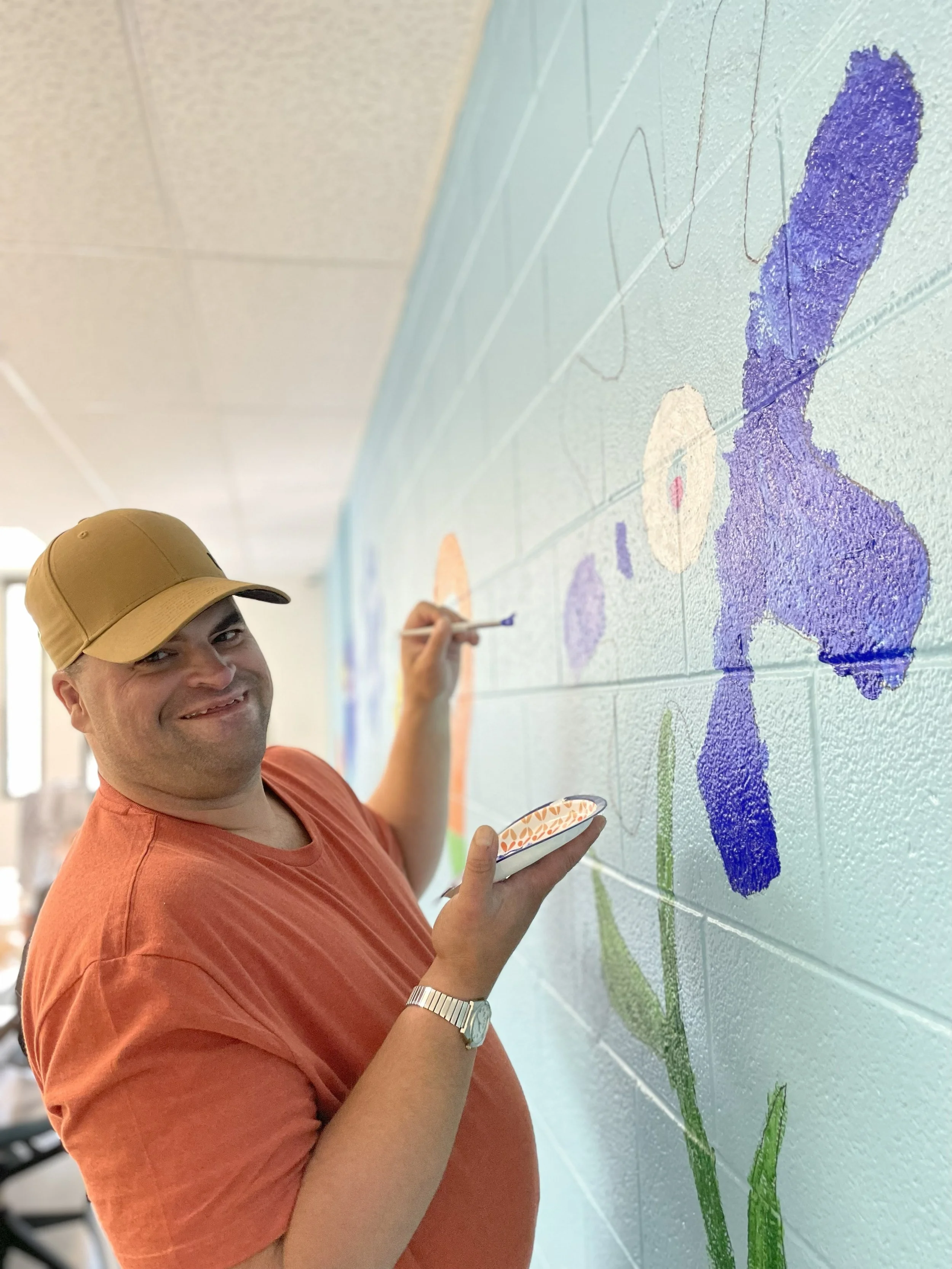  A young man is shown smiling as he paints a flower with a gear for a bloom on the wall in the NW Works Digital Literacy lab.  