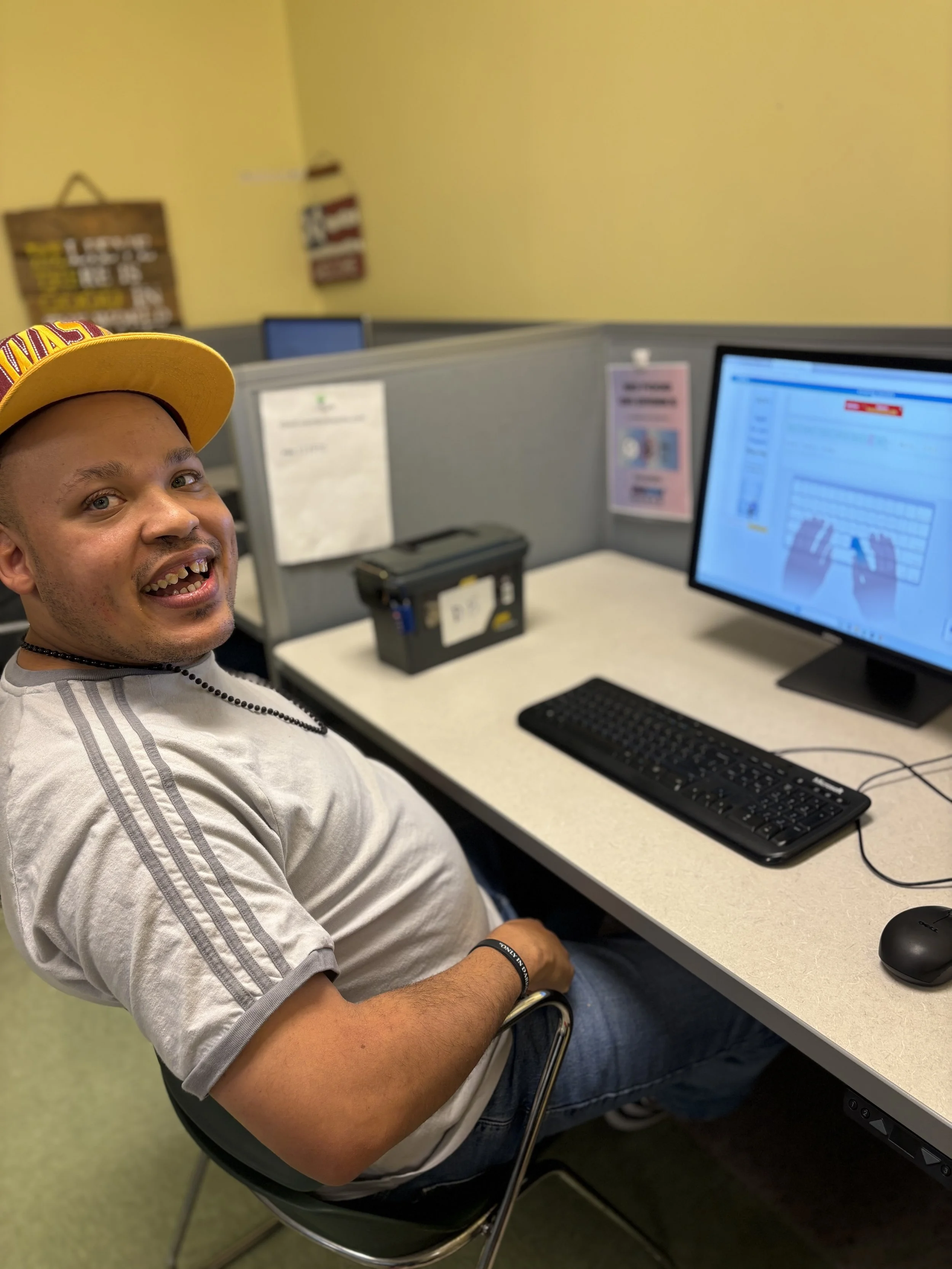A man is shown smiling at the camera as he pauses from his typing lesson on a computer.
