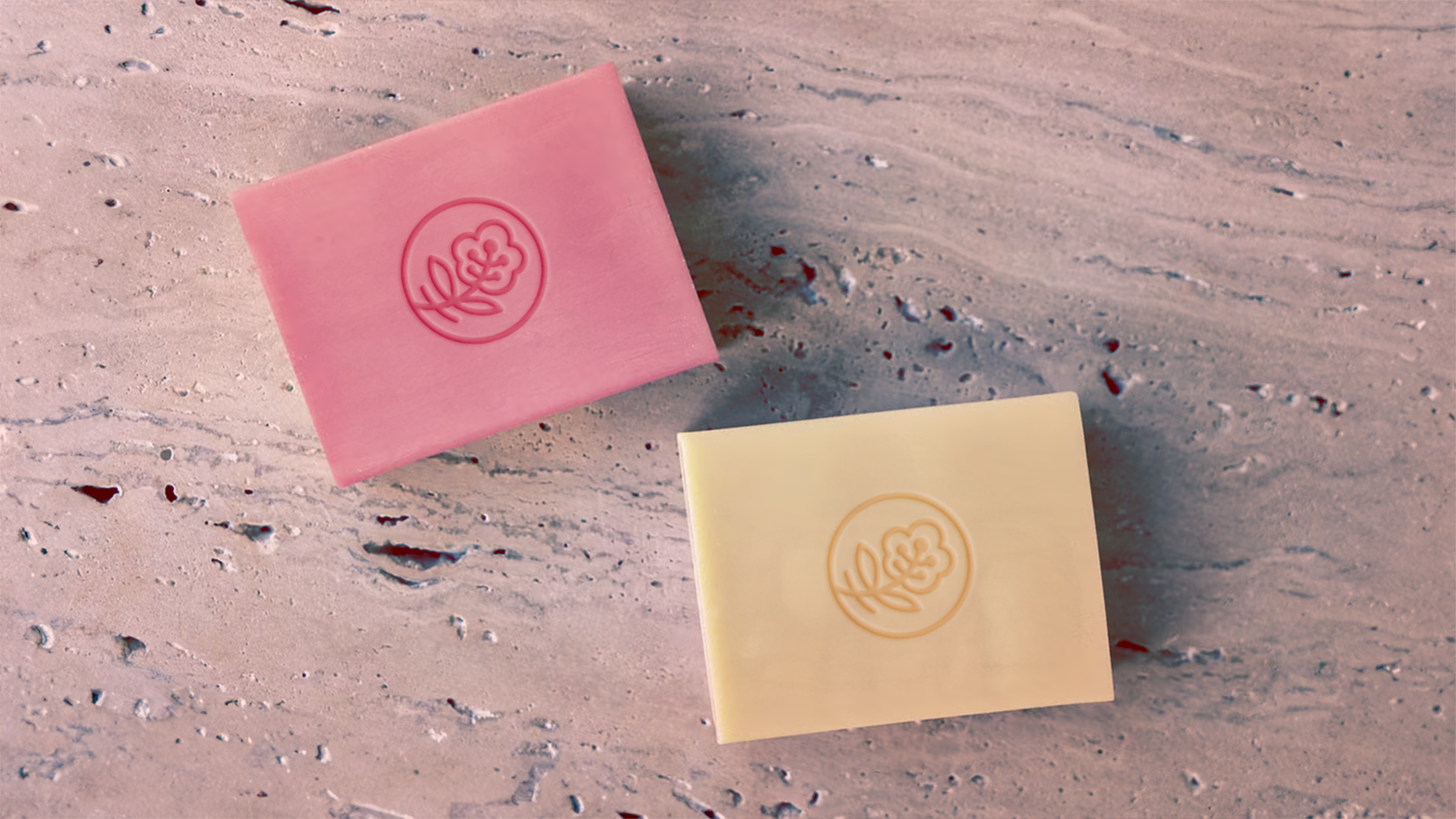 Luxury artisanal bar soap mockup on a stone background, featuring the Bare Essence flower logo debossed at the center of each bar.