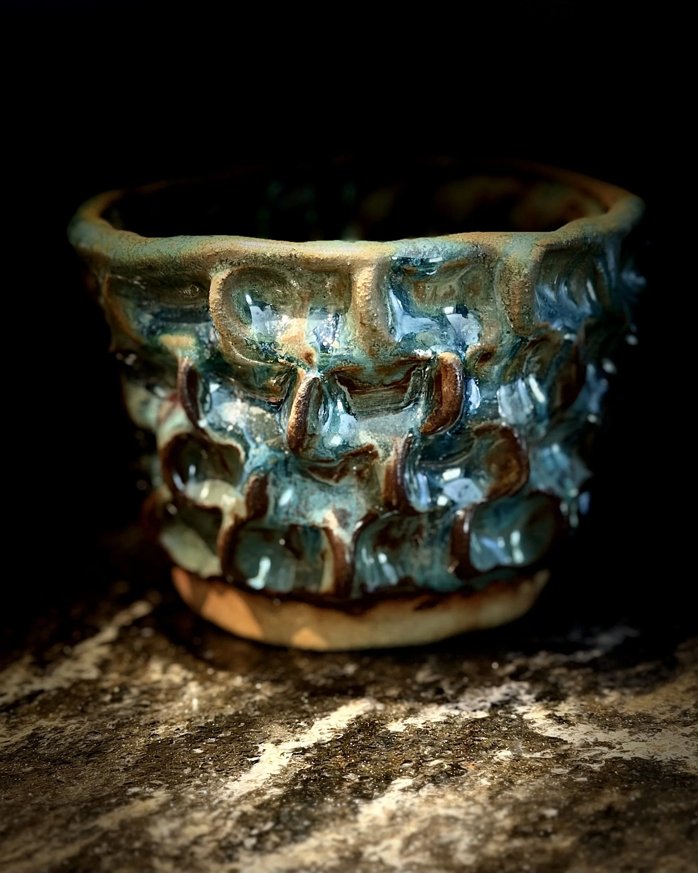Close-up of a ceramic bowl with a textured, uneven edge, sitting in a dark environment with lighting highlighting the bowl's glossy surface.