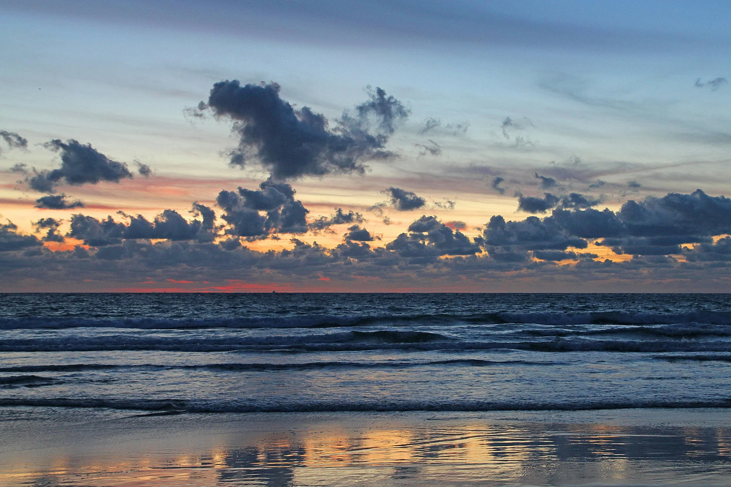 Dramatic ocean sunset with colorful skies painted in orange, purple, and blue hues, reflecting on the waves and wet sand, symbolizing peace and connection with nature.