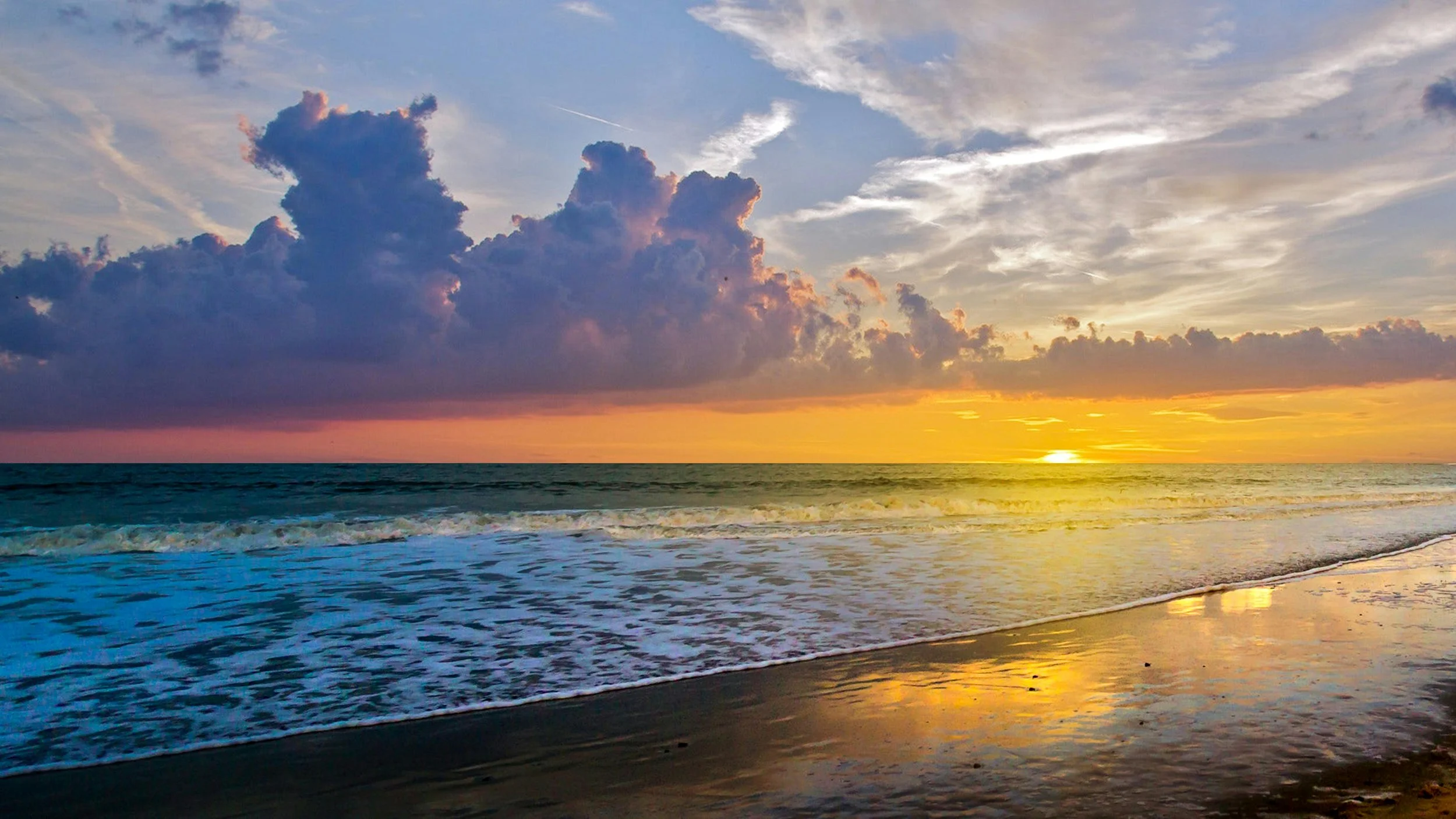 Golden sunset over the ocean with dramatic purple and orange clouds reflecting on the wet shoreline, evoking peace, renewal, and Habits for the Spirit.
