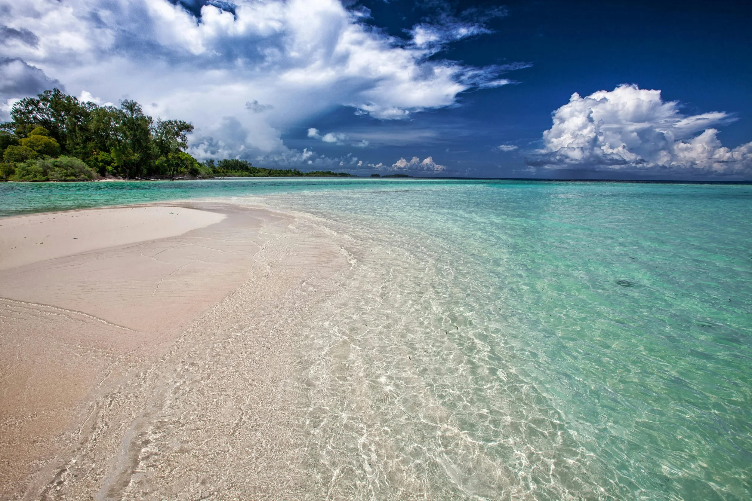 A pristine tropical beach with crystal-clear turquoise waters, soft white sand, and lush greenery under a dramatic sky, capturing the beauty of paradise.