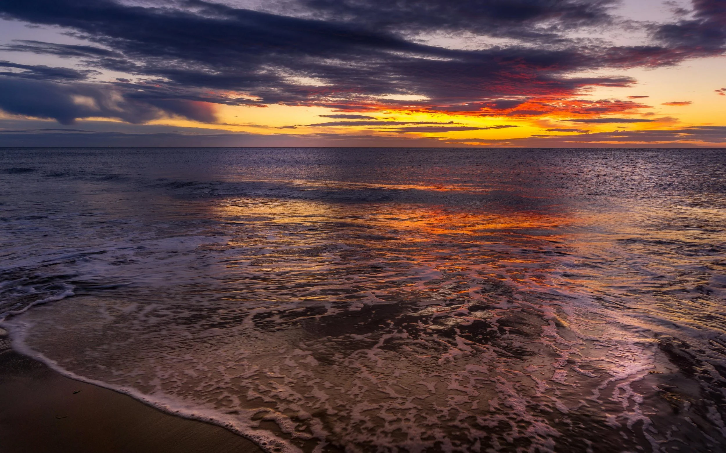 Colorful ocean sunset with dramatic clouds reflecting orange, purple, and golden hues on the gentle waves, evoking peace and Habits for the Spirit.