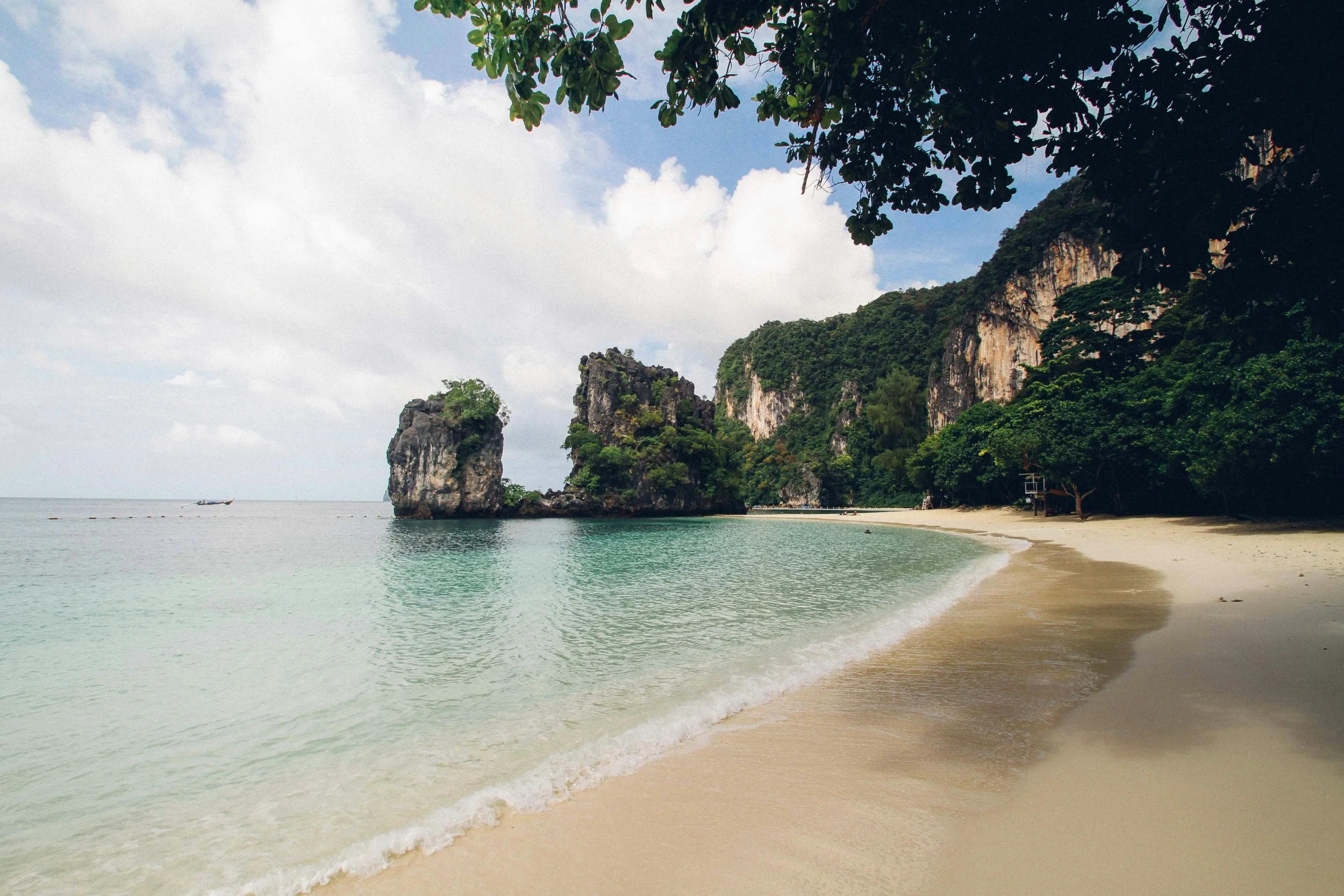 A tranquil tropical beach with turquoise waters, soft white sand, and dramatic limestone cliffs covered in lush greenery, showcasing the natural beauty of paradise.