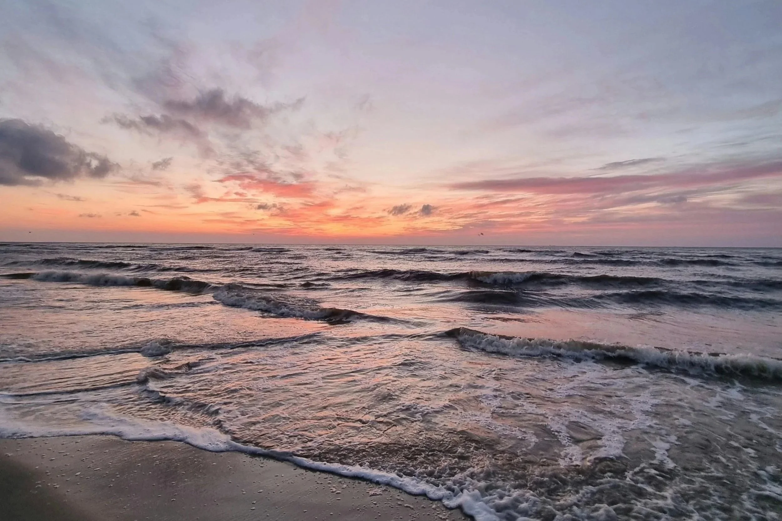 Peaceful ocean waves rolling onto the shore at sunset, with soft pastel skies reflecting on the water, evoking calmness and connection to nature.
