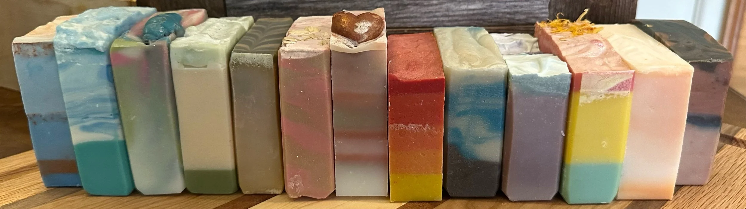 Three rows of handcrafted soap bars on a metal rack, with the first row being pink and white, the second yellow, and the third pink and green marbled.