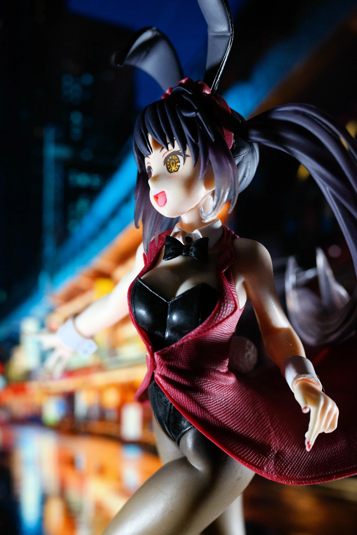 A stylized anime bunny girl figure in a red outfit is posed dynamically in the foreground, lit with dramatic directional lighting. Her face is sharply illuminated while the rest of her body falls into softer shadow. Behind her, a blurred nighttime ci
