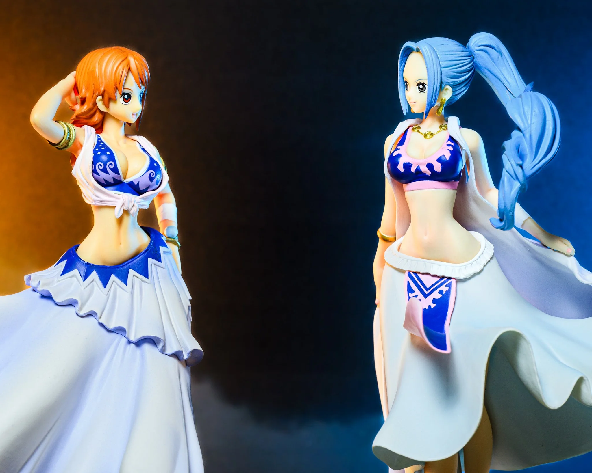 Two One Piece figures, Nami and Vivi, face one another beneath dramatic split lighting. Nami stands in warm orange light on the left while Vivi is illuminated by cool blue light on the right. Low-lying fog and a dark gradient background create a cine