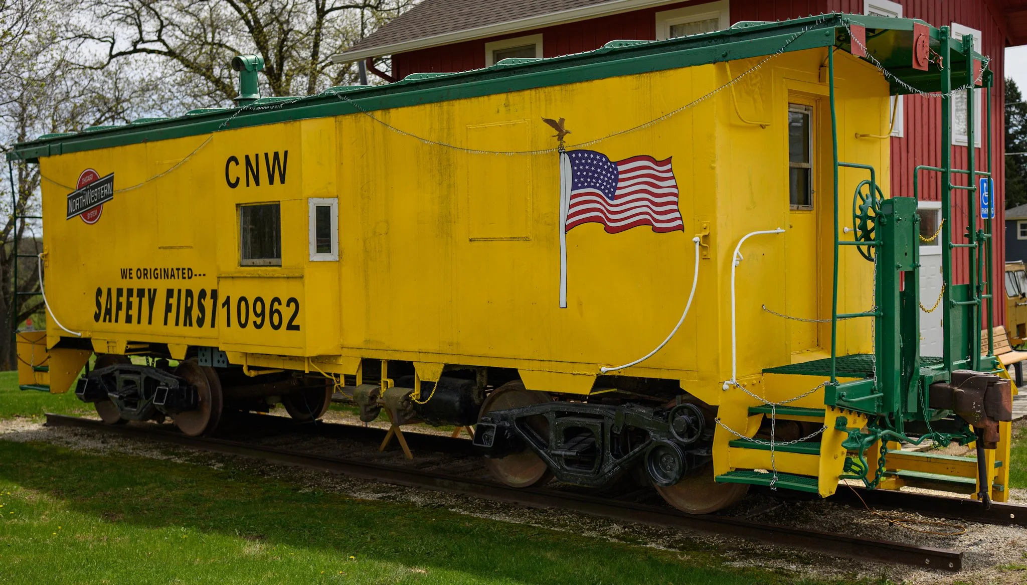 A bright yellow Union Pacific caboose stands on display in open daylight, its vivid paint, worn surfaces, and American flag emblem highlighting its preserved railroad heritage.