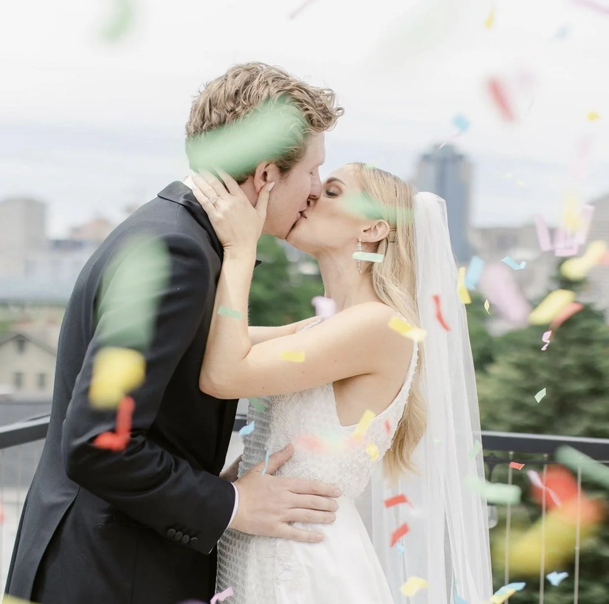 Bride and groom kissing at a wedding with colorful confetti.