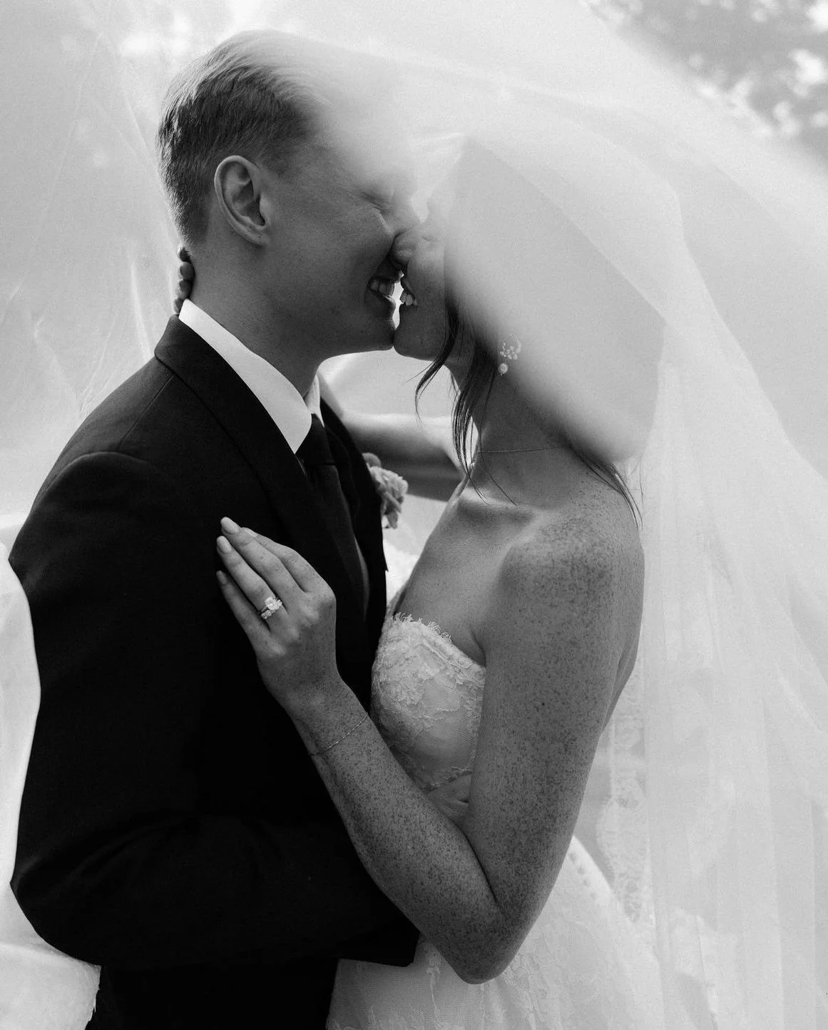 Bride and groom kissing under a veil in black and white.