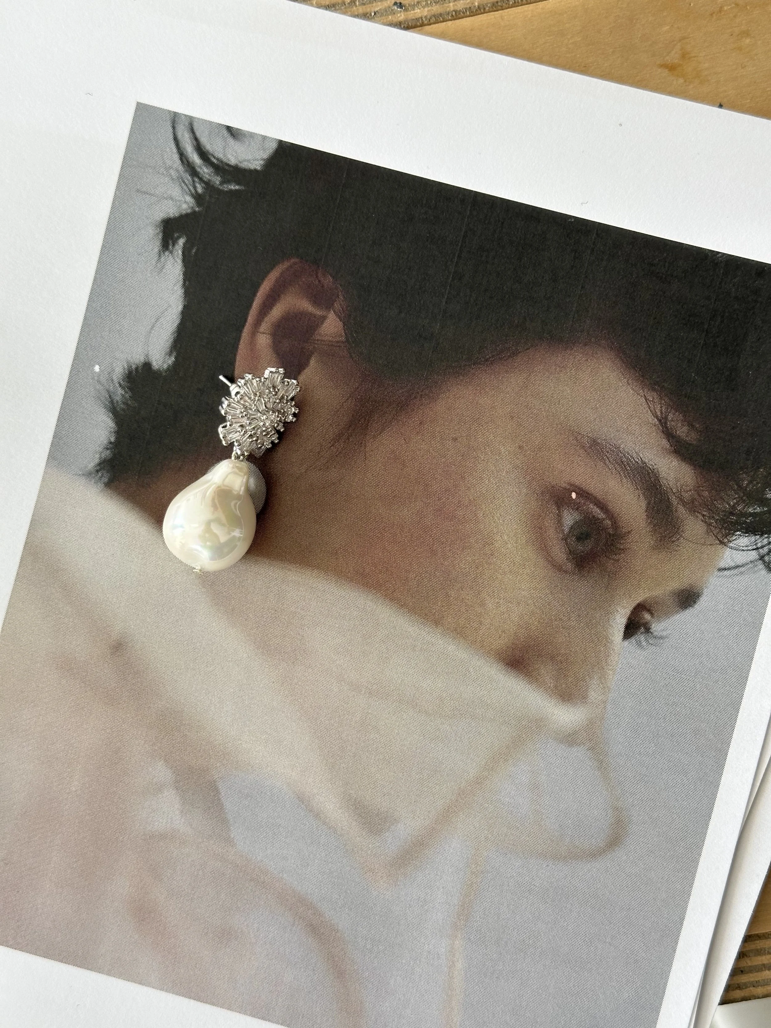 Woman with elegant earrings and hand near shoulder, wearing a white top, on a beige background.