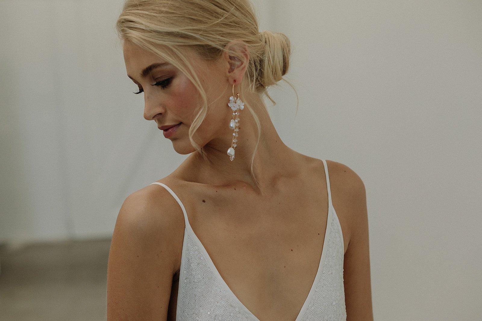 Woman in white dress wearing dangling earrings, hair in an updo.