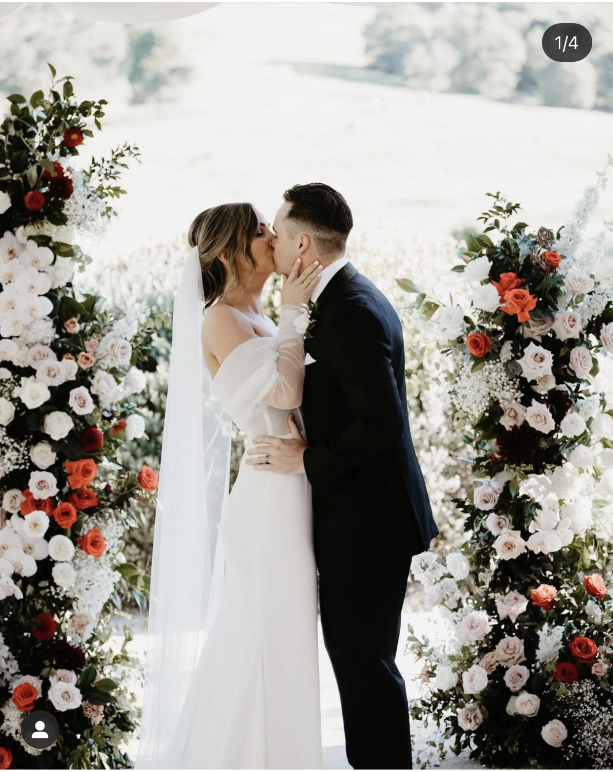 Bride and groom kissing at an outdoor wedding ceremony with floral arrangements.