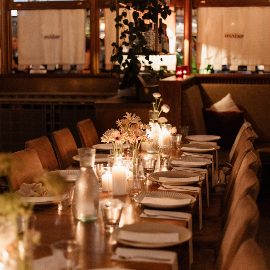 A dimly lit restaurant table decorated with pink flowers and candles, set with plates, glasses, and napkins.
