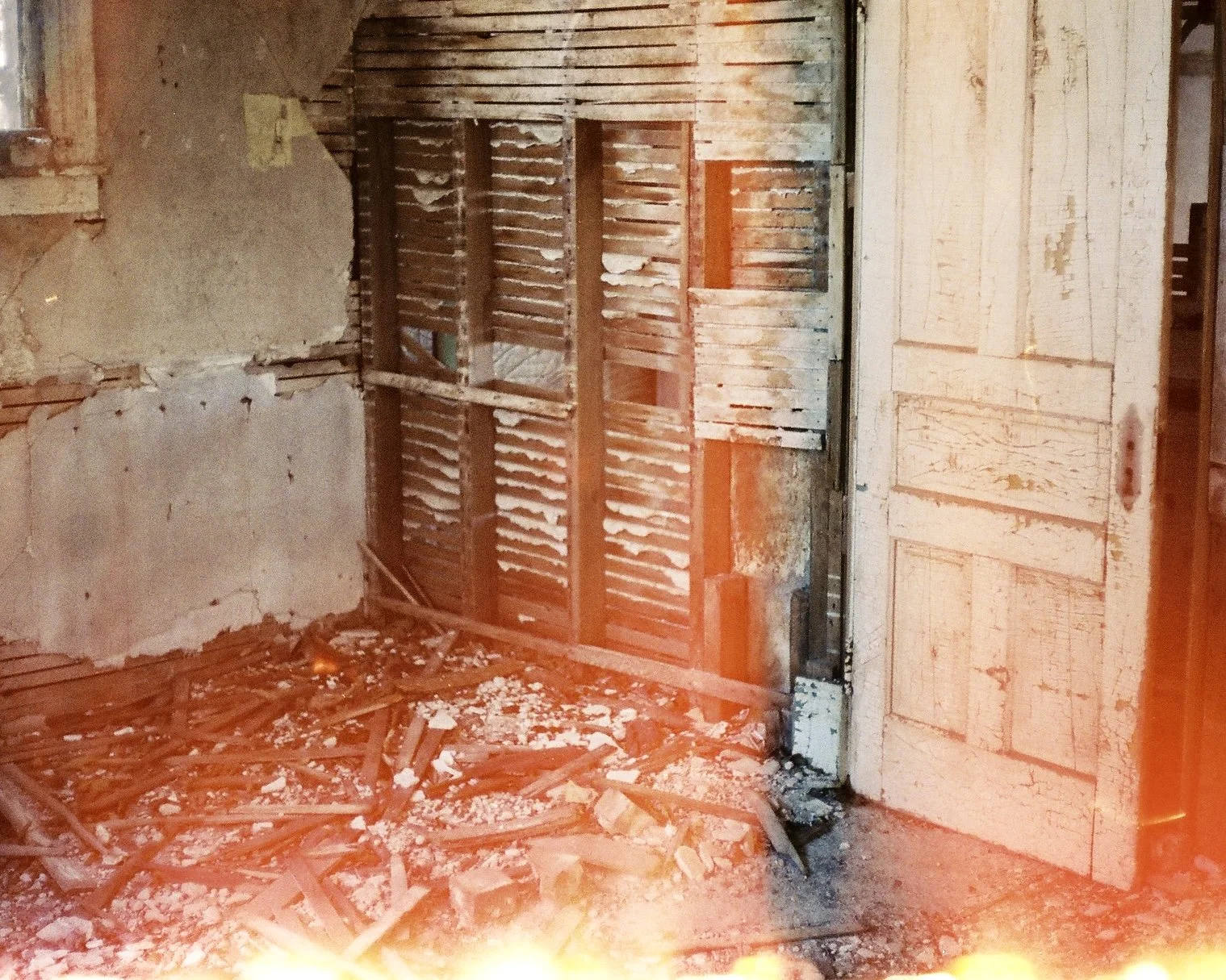 a camera glitch creates light leaks at the bottom of the image. The interior of an old wall has been partially dismantled, next to a door with no doorknob.