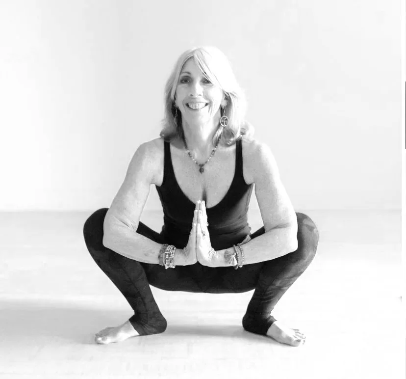 A woman smiling and posing with her hands on her hips, wearing a sleeveless top and jewelry, in black and white.