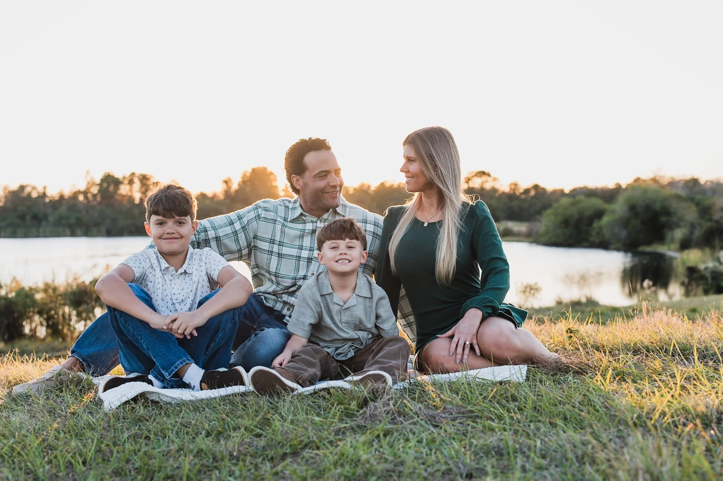 Mother, father, and two sons sitting on a blanket at sunset.