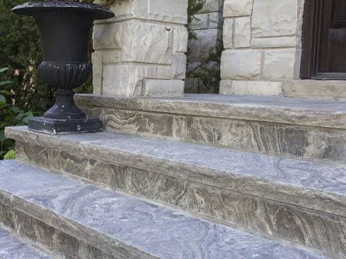 Stone steps with a black decorative planter on top, leading to a building with white brick walls and a window.