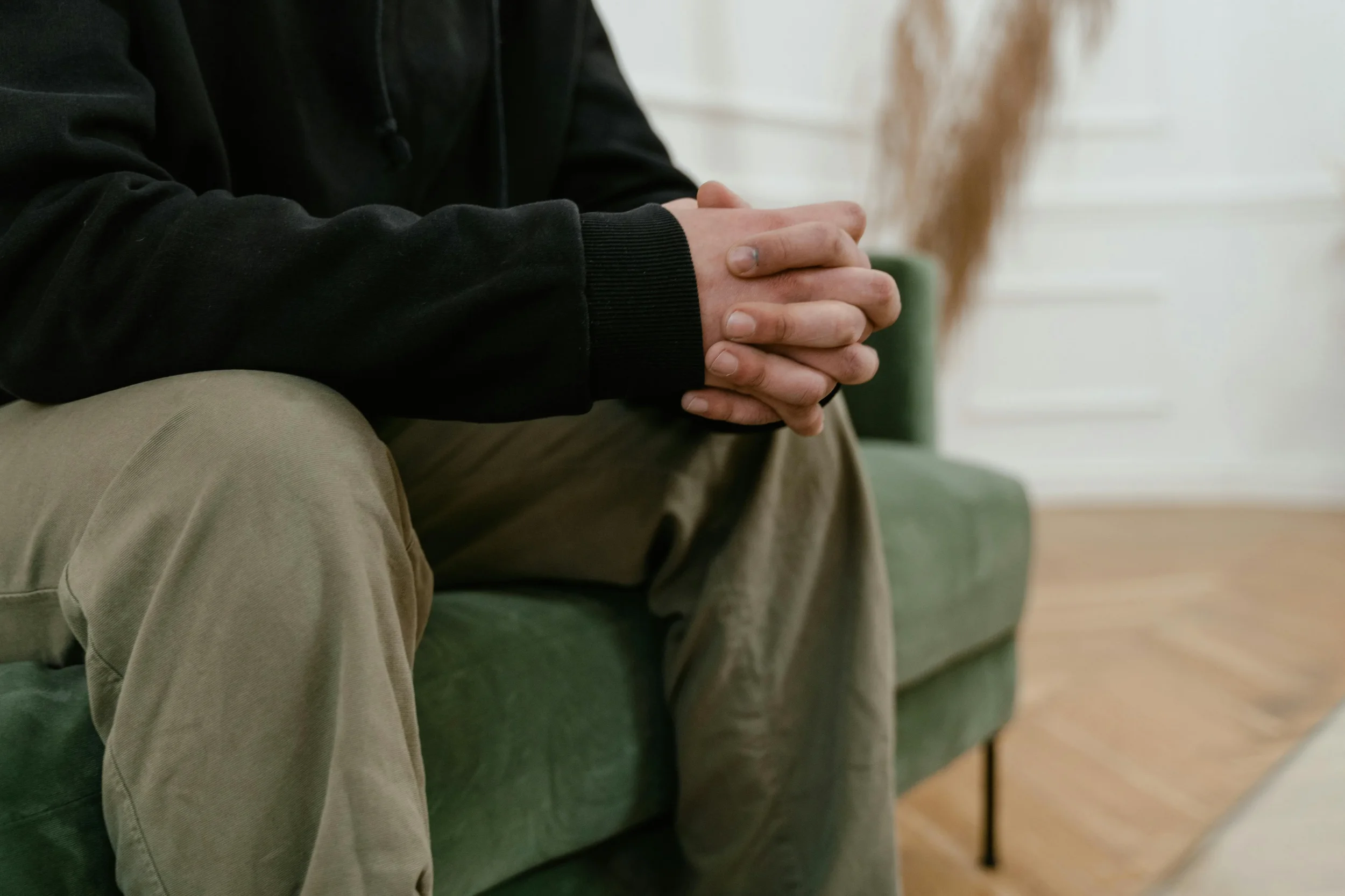 Man in Therapy sitting with hands clasped, showing signs of stress or deep contemplation.