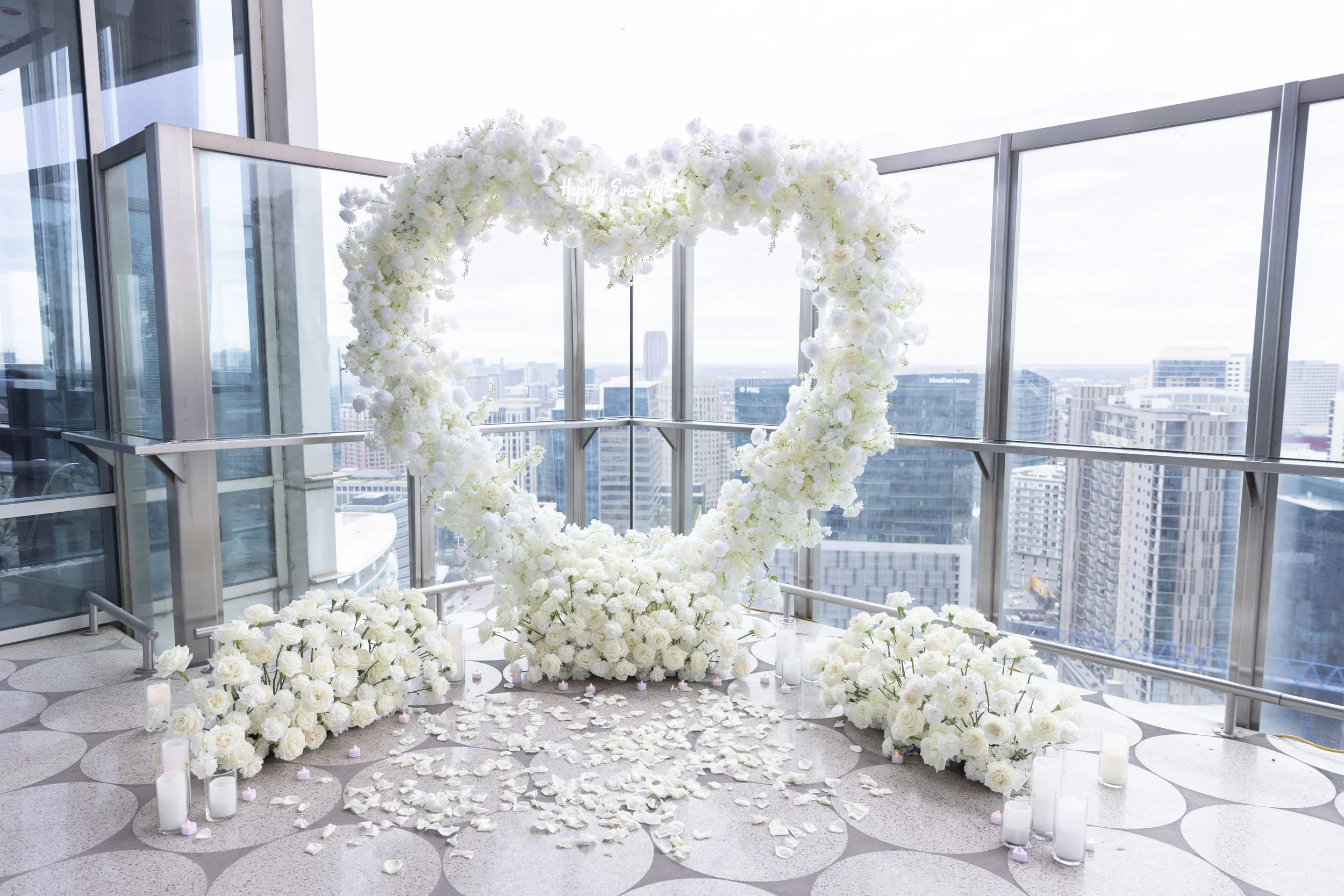 A proposal set up on a balcony in downtown Dallas with a white heart arch and white roses and candles.