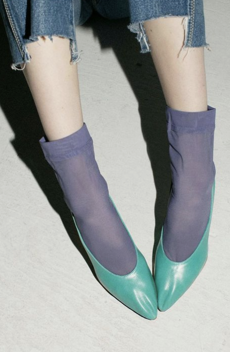 Person wearing ripped jeans, purple socks, and teal pointed-toe shoes.