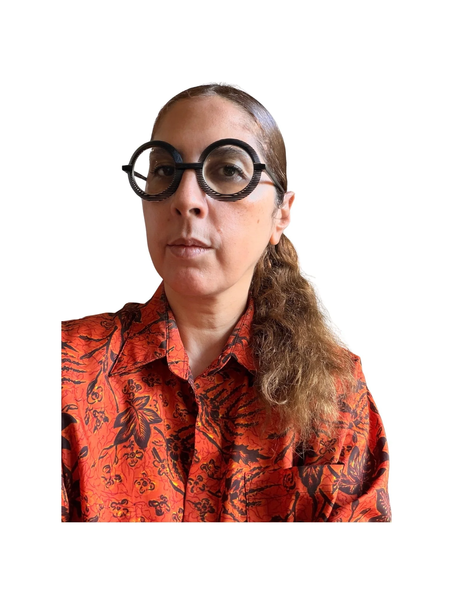 Woman with brown hair tied back wearing large circular glasses with striped black and white frames, and an orange patterned shirt with black floral and abstract designs.