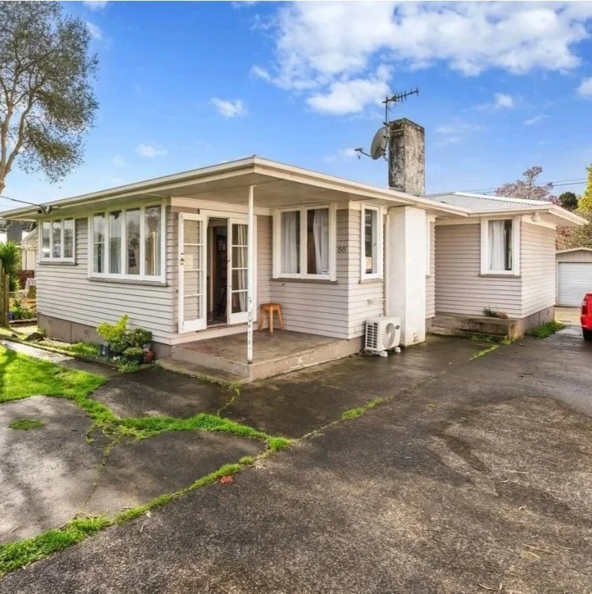 A single-story house with a white exterior, multiple windows, and a small front porch with a stool. Wolfe Property client investment property.