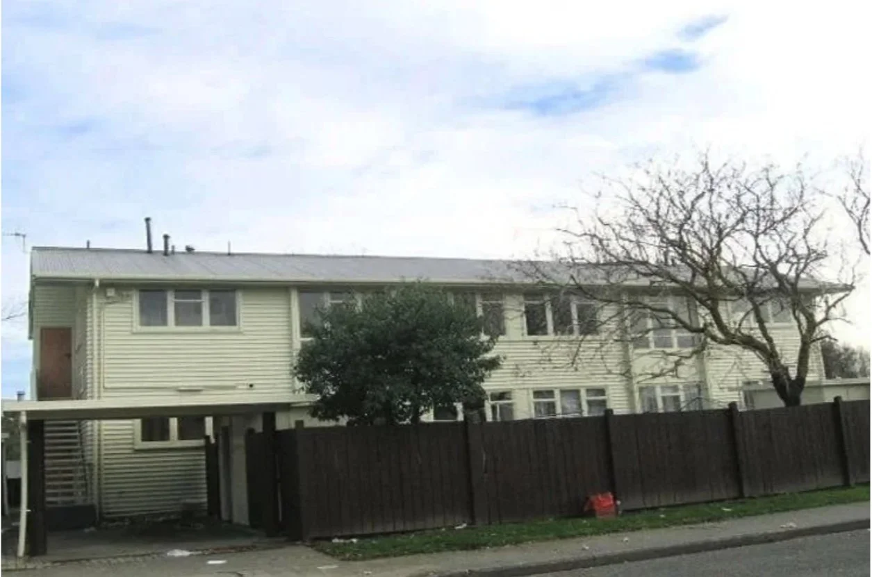 A two-story house with a beige exterior, brown fence, tree with no leaves, and a cloudy sky. Wolfe Property client investment property