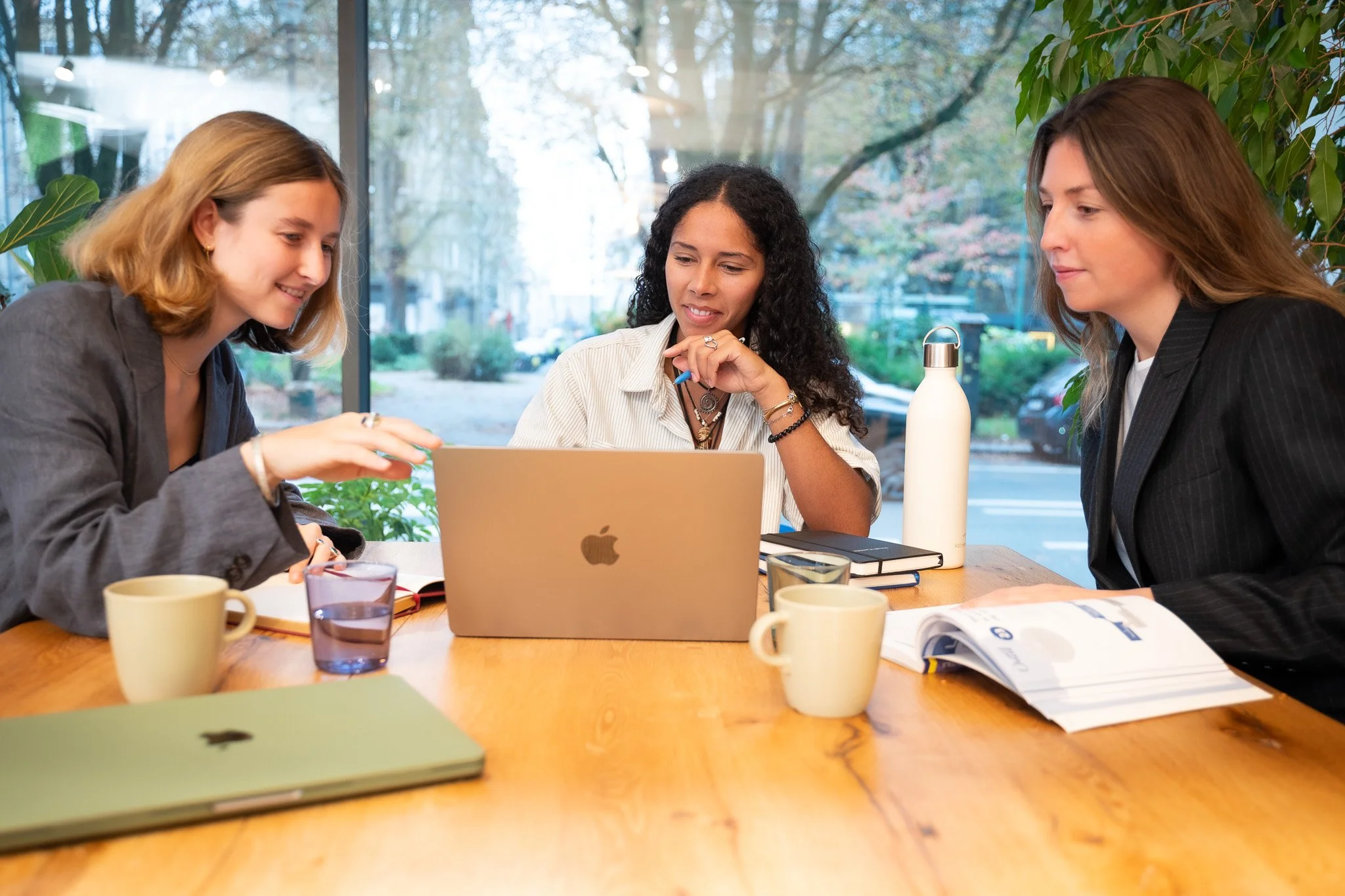 photo of three ladies blond and brown hair sitting on a table behind a macbook in a meeting