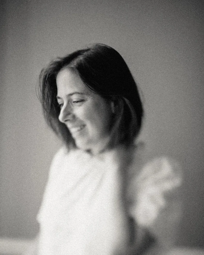 Portrait en noir et blanc d'une femme souriante avec les yeux presque fermés, regardant vers le bas, avec des cheveux bruns de longueur moyenne, portant un vêtement clair.