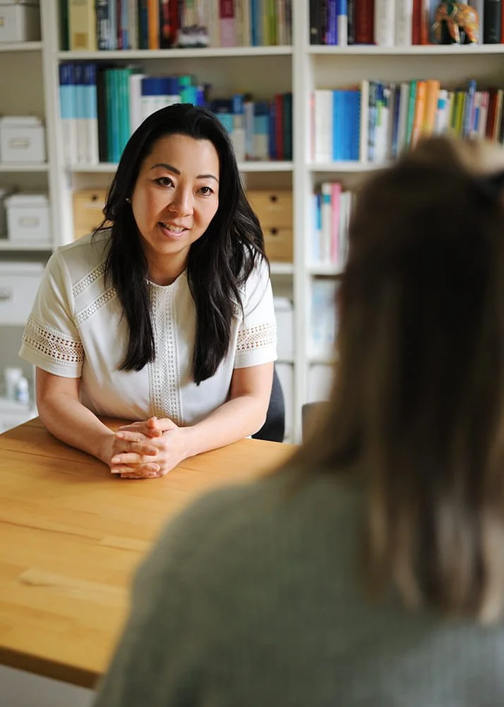 Zwei Frauen sitzen sich gegenüber, im Hintergrund ist ein Bücherregal und sie unterhalten sich