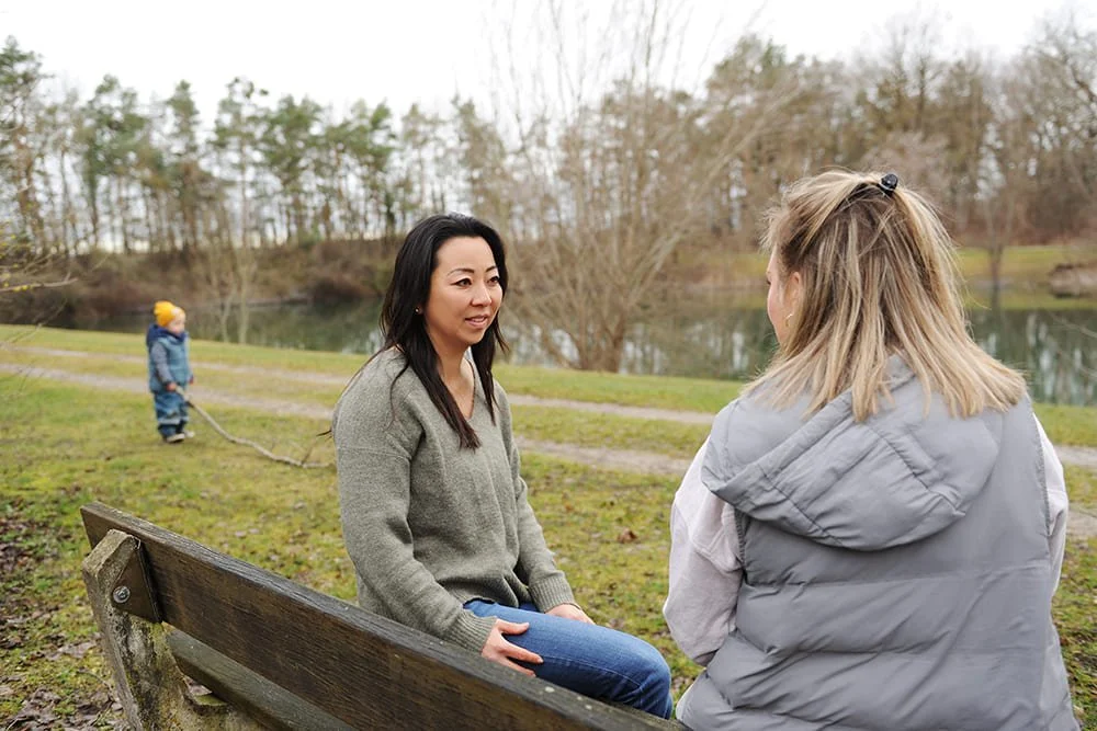 Zwei Frauen auf der Parkplatz in der Natur, ein Kind spielt im Hintergrund