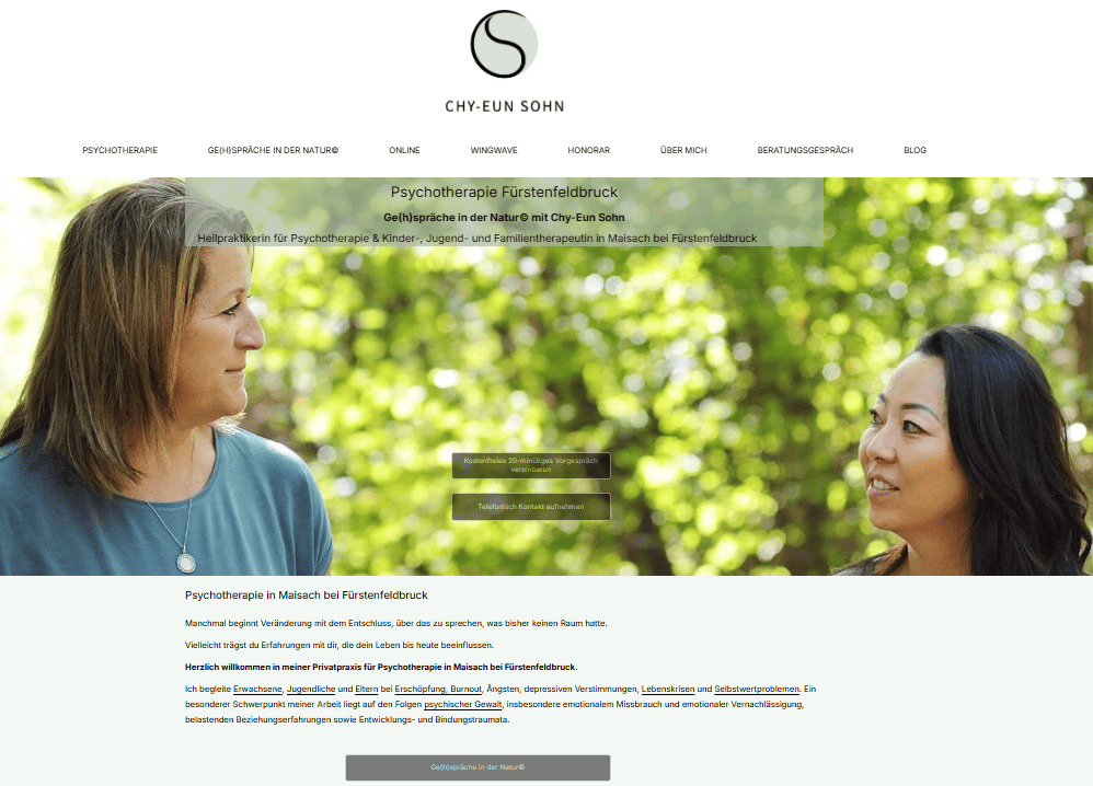 Zwei Frauen lächeln sich an, im Hintergrund ist grüne Natur zu sehen, eine Frau hat dunkelblinde schulterlange Haare und die andere sieht koreanisch aus und hat schwarzes volles und gewelltes Haar, Psychotherapie beim Gehen in der Natur in FFB