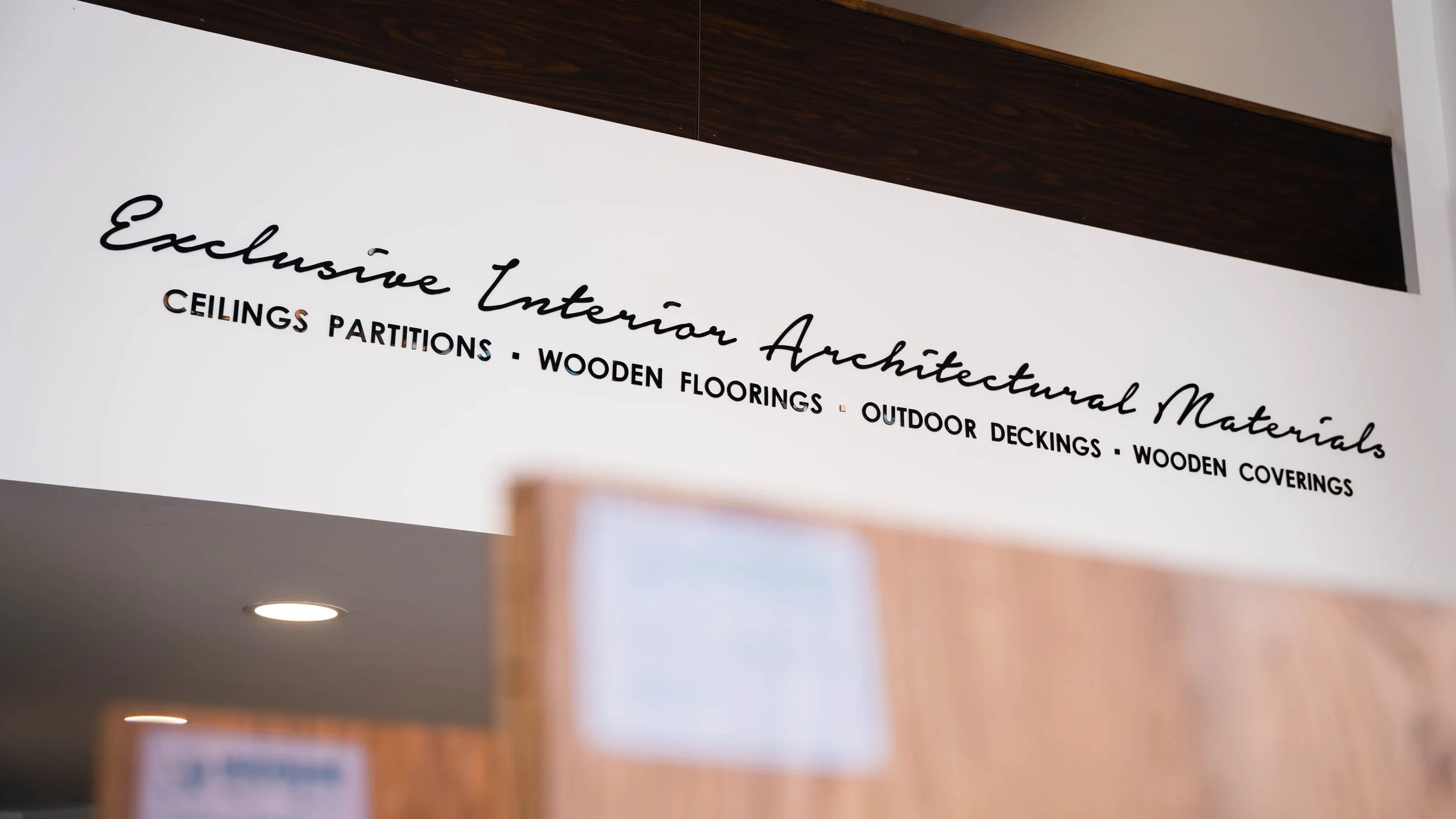 Sign that reads "Exclusive Interior Architectural Materials" with a list of products including ceilings, partitions, wooden floorings, outdoor deckings, and wooden coverings.